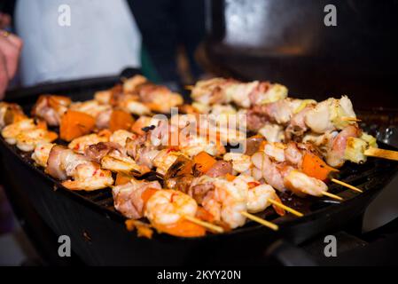 Lo shashlik (shish kebab) sugli spiedini sta cucinando sulla griglia. Fette di patate dolci, pancetta. Foto Stock