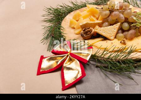 Spuntini di Natale su un rustico asse di legno con boa oro su sfondo di carta. Piatto di formaggi. Concetto di cibo di Natale. Foto Stock