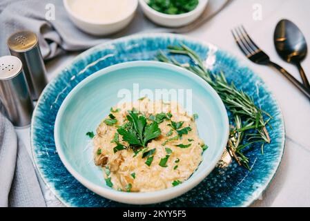 Porzione di risotto con formaggio grattugiato e pezzi di funghi. Il piatto è cosparso di foglie di prezzemolo tritate fresche. Foto Stock