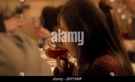 Primo piano di una giovane ragazza asiatica. Mangia e beve succo. La famiglia festeggia Natale, Capodanno o il giorno del Ringraziamento. Tavolo per le vacanze servito. Calda atmosfera di famiglia cena di Natale a casa. Foto Stock