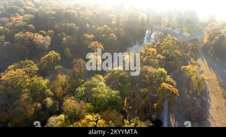 Vista aerea sul lago con colonne architettoniche e alberi con foglie giallo-verdi nel parco in una luminosa e soleggiata mattinata autunnale. Raggi di sole, luce solare rossa, sovraesposizione al sole. Sfondo naturale Foto Stock