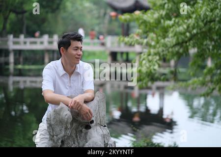 Giovane uomo cinese sorridente al parco all'aperto, vista laterale che guarda lontano Foto Stock