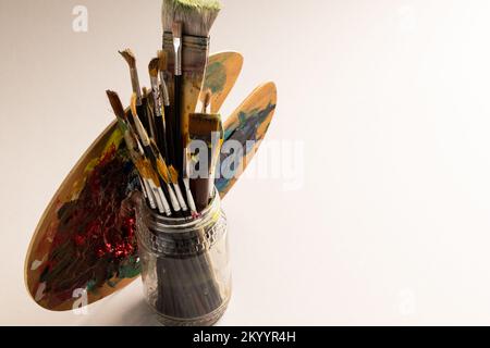 Composizione vasetto di pennelli e palette di pittura su sfondo bianco Foto Stock