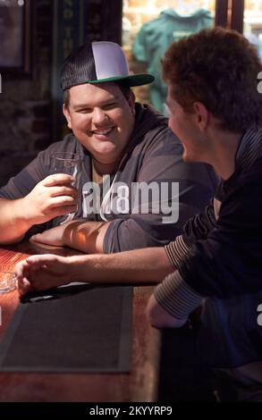 Avere una pinta con il suo amico. Due amici sorseggiano un drink al bar locale. Foto Stock