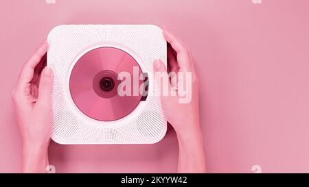 Colore dell'anno 2023 Viva Magenta. L'immagine con le mani che reggono l'elegante lettore CD portatile con disco è colorata in pantone. Nuovo colore moda. Foto Stock