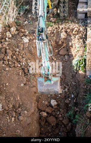 Il mini escavatore scava una trincea per posare i tubi. Primo piano di un escavatore che scava una trincea profonda. Un escavatore scava una trincea nella campagna per posare un Foto Stock