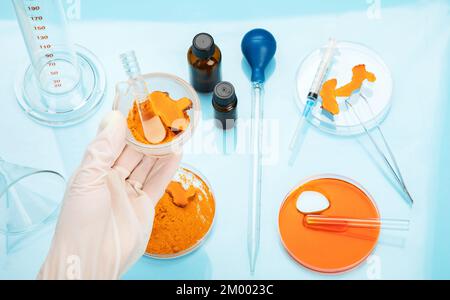 Ricerca medica delle proprietà curcuma con l'aiuto di attrezzature di laboratorio, donna in guanti di prova curcuma polvere. Vista dall'alto. Foto Stock