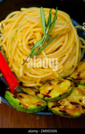 Spaghetti italiani con salsa di zucchine su padella di ferro su tavola di legno Foto Stock