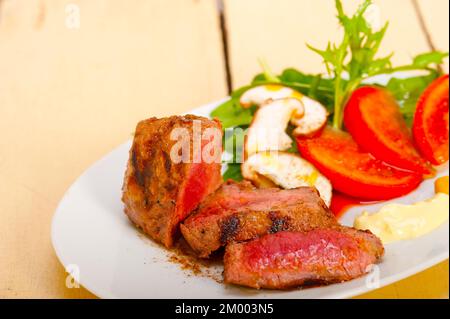 Filetto di manzo mignon grigliato con verdure fresche sul lato, funghi pomodoro e insalata di rucola Foto Stock