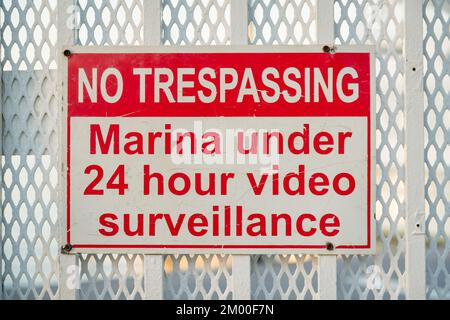 Destin, Florida - No Trespassing, Marina sotto il cartello di videosorveglianza 24 ore su 24. Primo piano di un cartello sulle ringhiere metalliche verniciate con estensione in acciaio inox Foto Stock