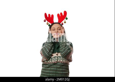 Donna deliziosa in maglione verde e cervi corna cerchio, mette le mani sul suo volto, godendo prossime vacanze di Natale Foto Stock