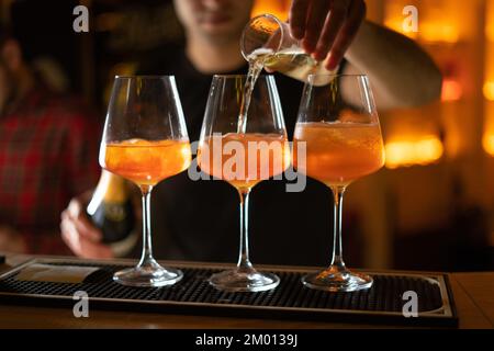 Chiudete tre bicchieri di cocktail al bar. Il barista versa un bicchiere di spumante con Aperol. Spazio di copia Foto Stock