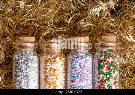 Nonpareils in piccole bottiglie di vetro, su capelli d'angelo dorati. Inverno e natale mix colorati di confetteria commestibile di piccole palle di zucchero. Foto Stock