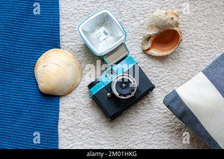 Fotocamera a pellicola di plastica, conchiglie marine e cuscino spogliato su uno sfondo in tessuto testurizzato Foto Stock