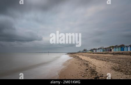 Capanne sulla spiaggia di Mersea Island in Essex. Moody, cielo nuvoloso e foto a lunga esposizione. Foto Stock