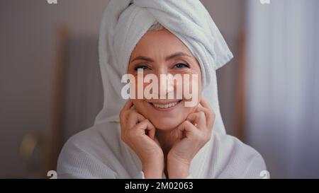 Primo piano ritratto vecchio di mezza età anziano senior caucasico sorridente donna faccia donna in accappatoio da bagno con asciugamano sulla testa con pelle occhi patch per Foto Stock