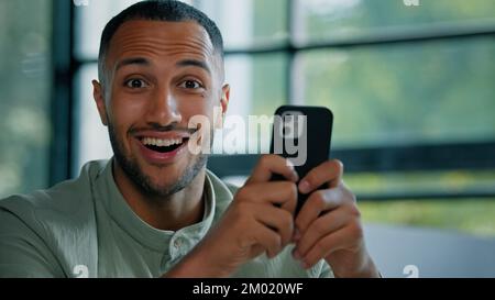 Emotivo uomo uomo d'affari africano uomo imprenditore ragazzo cercando telefono cellulare lettura notizie messaggio e-mail risultato stupito meraviglia scioccato Foto Stock