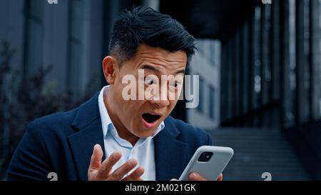 Felice eccitato 50s anni vincitore uomo d'affari leader uomo ha business chat in smartphone ricevere buone notizie vincendo con cellulare grande grande vittoria Foto Stock