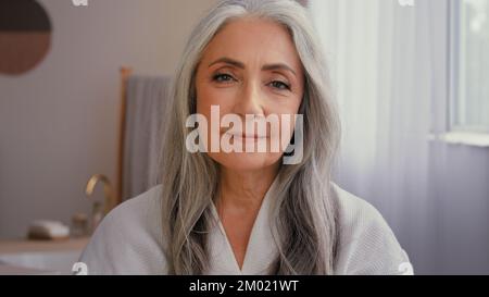 Ritratto interno vecchio caucasico 50s modello senior grigio-capelli donna matura 60s donna in bagno mostrando vaso di anti-invecchiamento cosmetico naturale organico Foto Stock