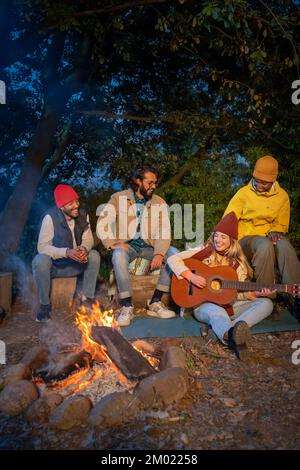 Amici di gruppo che si divertono a ridere e cantare intorno al bonfire campeggio concetto di amicizia giovanile Foto Stock