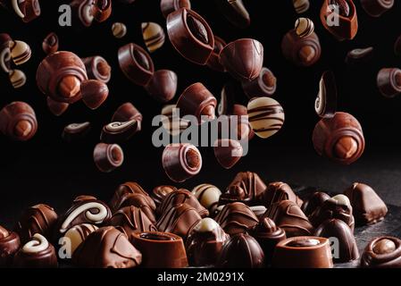 caramelle al cioccolato con vari ripieni, dolci di fondo. Levitazione o volo di cioccolatini bruni dolci o confit su uno sfondo nero scuro Foto Stock