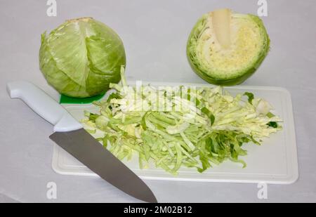 diversi cavoli, uno tagliato finemente su una tavola da taglio, un altro tagliato a metà e uno intero Foto Stock