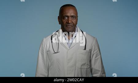 Maturo sicuro medico felice in piedi in uno studio di sfondo grigio con le braccia incrociate felice sorridente afroamericano uomo medico terapeuta professionista Foto Stock