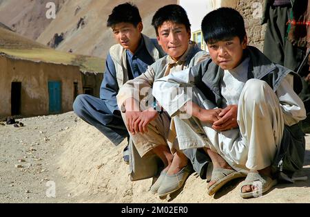 Provincia di Syadara (Siyah Darah), Bamyan (Bamiyan) / Afghanistan: Tre giovani afghani seduti e schiacciati in linea su una strada nell'Afghanistan centrale. Foto Stock