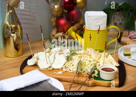 Diverse varietà di formaggio su un tavolo di legno, antipasti freddi sul tavolo delle feste. Formaggio cecile, formaggio suluguni, formaggio duro, anacardi. Foto Stock