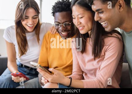 Gruppo di giovani amici adolescenti multietnici che usano il telefono cellulare insieme a casa Foto Stock