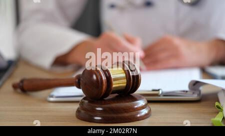 Gavel di legno del giudice sul primo piano della tabella e medico sfocato che fa la documentazione in clinica medica. Foto Stock