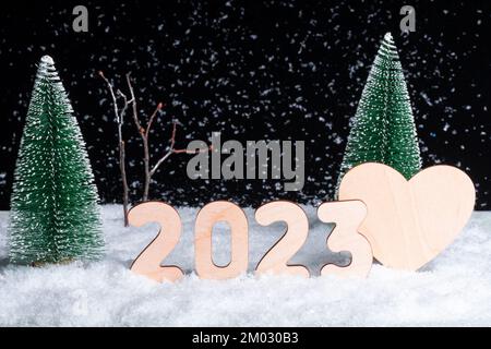 Carta del Capodanno creativo. Una composizione di numeri di legno dell'anno 2023 e un cuore in una foresta innevata durante una nevicata di notte. Amore in th Foto Stock