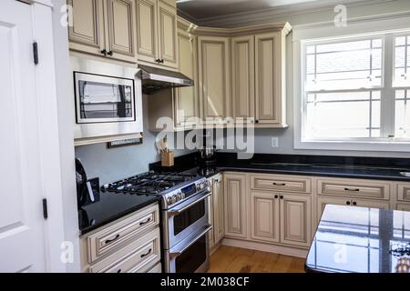 Una nuova cucina color crema con ripiani in granito nero e pavimenti in legno e elettrodomestici in acciaio inossidabile Foto Stock