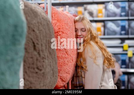 Una ragazza adolescente preme la guancia contro un soffice cuscino per controllare le sensazioni e scegliere quella giusta. nel negozio. La scelta dei letti o. Foto Stock