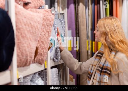 Una ragazza adolescente tocca la mano sopra il tappeto morbido nel negozio. La scelta di biancheria da letto o elementi decorativi per la casa in un negozio di specialità. Foto Stock