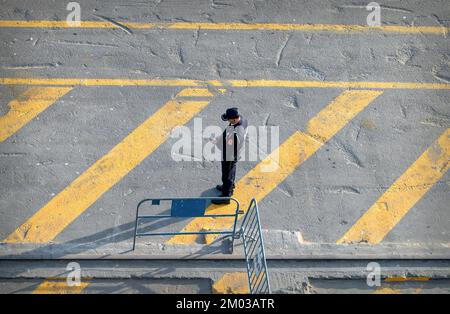 Poliziotto, con il telefono cellulare in mano, in piedi su una strada segnata in giallo. Foto Stock