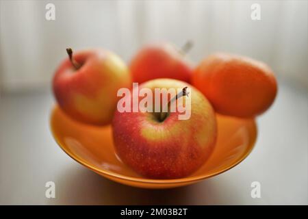 mandarino e tre mele rosse in piatto arancione sul tavolo d'argento. Foto Stock