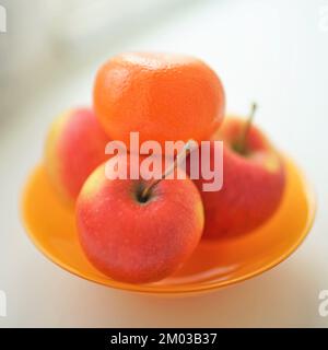 mandarino e tre mele rosse in piatto arancione sul tavolo di wite. Foto Stock