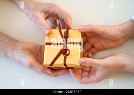 Le mani femminili tengono e danno un regalo imballato piacevole. Foto Stock