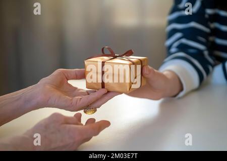 Le mani femminili tengono e danno un regalo imballato piacevole. Foto Stock