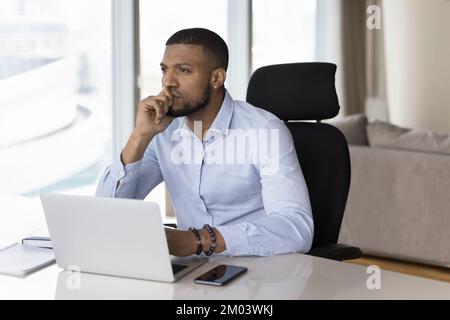 Felice imprenditore freelance africano millenario che guarda lontano dall'ufficio Foto Stock