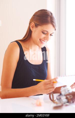 Invio di alcune foto. Una giovane donna sorridente che legge l'indirizzo su una busta con una macchina fotografica vintage posta in primo piano. Foto Stock
