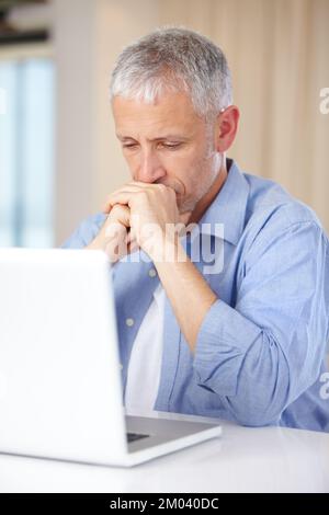 Qual è il modo migliore per inviare questa e-mail Un uomo maturo nel profondo del pensiero mentre si siede al suo laptop. Foto Stock