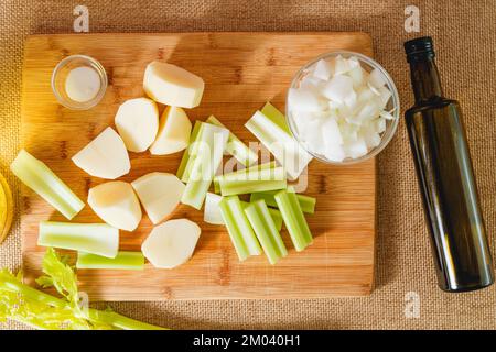 Verdure crude, come bastoncini di sedano, patate, cipolla tritata, olio d'oliva, sale, e brodo primo piano sul tavolo da cucina. Ingredienti per un sou di sedano Foto Stock