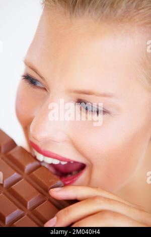 Rompere la sua dieta. Bella giovane donna godendo di un delizioso pezzo di cioccolato con un sorriso. Foto Stock