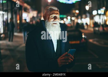 Happy Senior Hippster uomo utilizzando il telefono cellulare all'aperto in inverno notte - Focus sul viso Foto Stock