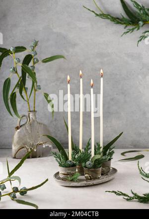 Decorazioni natalizie con quattro candele bianche avvento stretto e foglie di eucalipto. Arredamento fatto a mano. Messa a fuoco selettiva. (Eucalipto globulo) Foto Stock