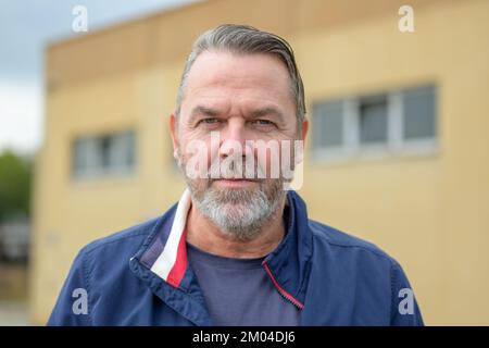 Uomo di mezza età che guarda la telecamera con uno sguardo poppa all'esterno di fronte ad un edificio giallo Foto Stock