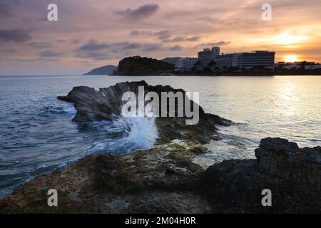 Santa Eulalia al tramonto con un'onda che si tuffa sulle rocce, Ibiza, Isole Baleari, Spagna. Foto Stock