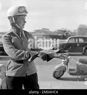 Negli anni '1950s. Una giovane donna vista su uno scooter Puch di origine tedesca. L'autista femminile indossa i tipici abiti e accessori per motociclette del decennio, casco, giacca, cintura renale e guanti. Svezia 1955 Foto Stock